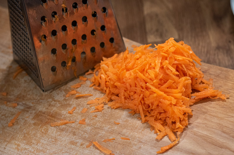 Grated carrot on a chopping board next to a grater