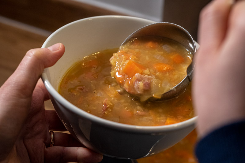 Lentil and bacon soup being served into a bowl with a ladle