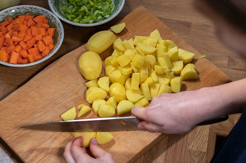 Potatoes being chopped on a board next to chopped carrot and leek
