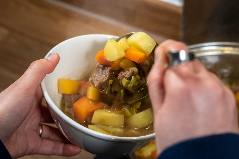 Beef stew being served in a bowl with a ladle