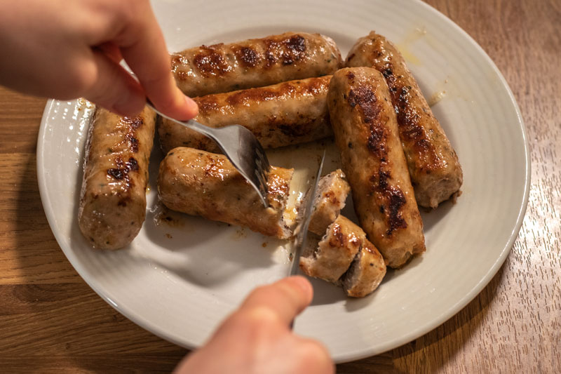 Cooked sausages being sliced with knife and fork
