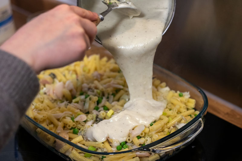 White sauce being poured over the pasta, fish and veg mix